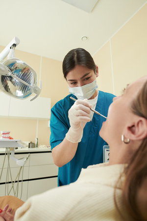 Young adult woman dentist examining mouth of young adult Caucasian woman patient using dental instrument in modern dental clinic, both focused on dental procedureの写真素材