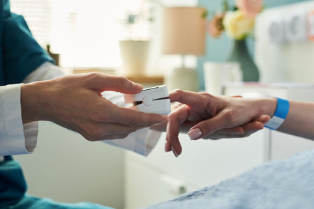 Caucasian middle aged woman lying in hospital bed receiving care from medical professional, nurse placing pulse oximeter on patient finger, healthcare setting visible in backgroundの写真素材