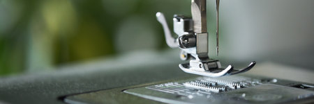 Close up showing metal presser foot and needle of sewing machine positioned above needle plate, focusing on mechanical details and precision components in textile equipmentの写真素材
