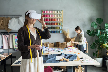 Caucasian young adult woman standing in workshop wearing virtual reality headset, holding...