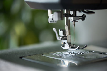Close up showing sewing machine needle and presser foot positioned above metal plate, focusing on mechanical details of equipment used for textile or garment productionの写真素材
