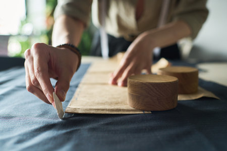 Caucasian young adult woman marking fabric with tailor chalk while working on sewing project, hands visible arranging pattern pieces and drawing lines on textile in workshop settingの写真素材