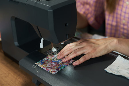 Caucasian young adult woman sewing colorful fabric with sewing machine, hands guiding material under needle, partial body visible, focusing on textile crafting processの写真素材