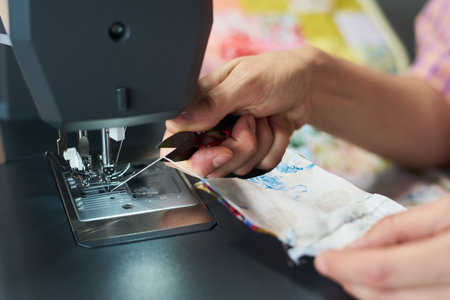 Caucasian woman using sewing machine, holding fabric and guiding needle with hands, focusing on precise stitching process, close up of hands and textile workの写真素材