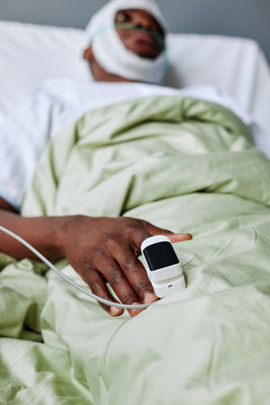 Vertical selective focus shot of young Black man with head injury lying in hospital bed with pulse oximeter on his fingerの写真素材