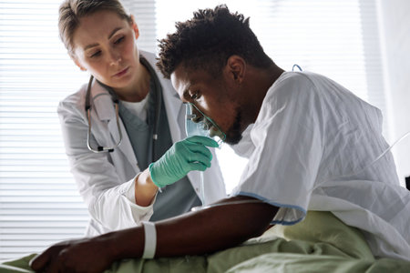 Young African Amercian man suffering problems with heart or lungs sitting on bed in hospital ward getting artificial ventilation therapyの写真素材