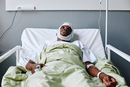 Horizontal shot of injured Black man with bandage on his head lying in hospital bed having IV therapy looking at ceilingの写真素材