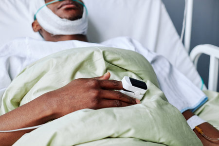 Cropped shot of unrecognizable young Black man with head injury lying in hospital bed with pulse oximeter on fingerの写真素材