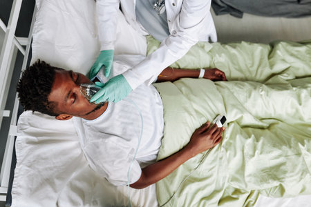 From above view of unrecognizable doctor changing mechanical ventilation mask for young Black patient in comaの写真素材