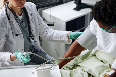 High angle view of professional doctor checking health state of Black patient in hospital ward measuring his blood pressureの写真素材