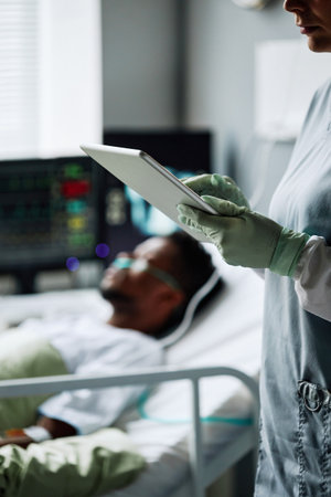 Vertical shot of female doctor checking her patient in hospital ward making notes in online medical record on digital tabletの写真素材