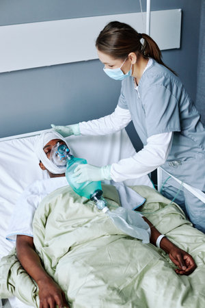 Vertical high angle view shot of Caucasian nurse wearing mask on face doing artificial ventilation for injured young Black manの写真素材