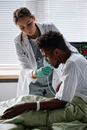 Vertical shot of professional medical worker giving young male patient artificial ventilation mask in hospital wardの写真素材