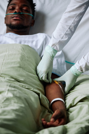 Vertical shot of young Black patient lying in hospital bed with eyes closed getting intravenous therapyの写真素材