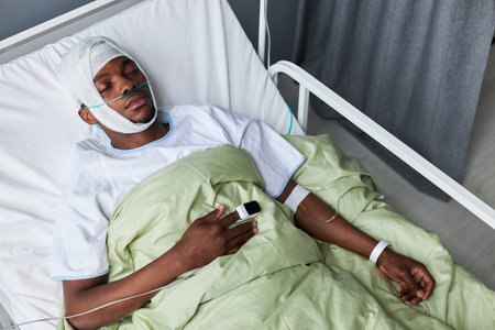 High angle view of young African American man with nasal cannula and pulse oximeter on finger spending days in coma after severe head injuryの写真素材