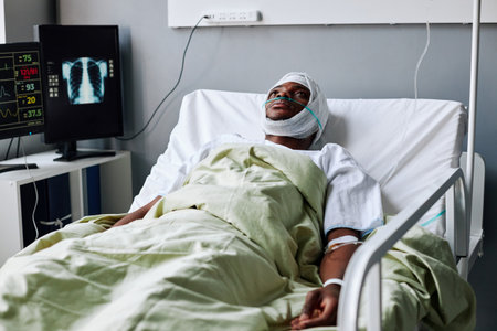 Horizontal shot of injured young African American man with bandage on head and nasal cannula lying in bed in hospital wardの写真素材