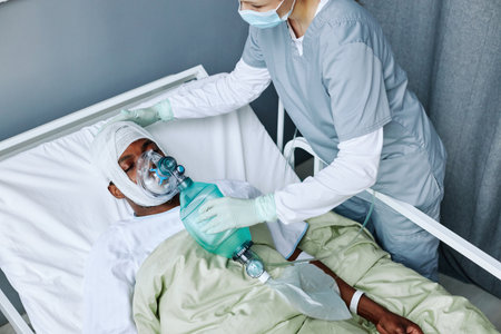 HIgh angle view of Caucasian nurse working in modern hospital doing artificial ventilation for young Black man with head injuryの写真素材