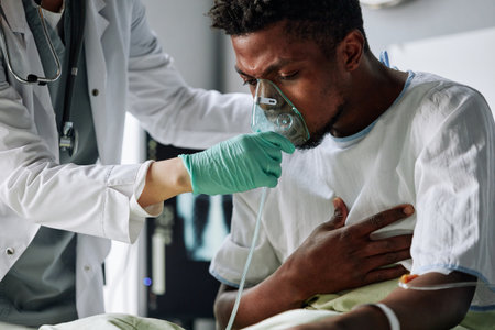 Young Black man suffering problems with heart or lungs sitting on bed in ward getting mechanical ventilation therapyの写真素材