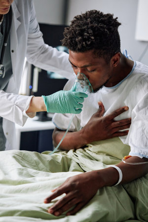 Careful doctor helping young Black patient with heart or lungs problems giving him mechanical ventilation maskの写真素材