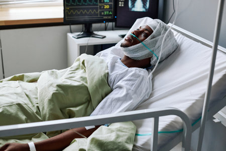 Horizontal shot of young Black man with nasal cannula and bandage on head lying in hospital bed after injury or surgeryの写真素材