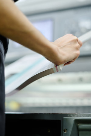 Selective focus close-up of unrecognizable female worker holding pile of printed productionの写真素材