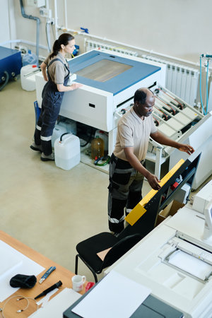 Vertical high angle view long shot of two ethnically diverse people working in modern printing houseの写真素材