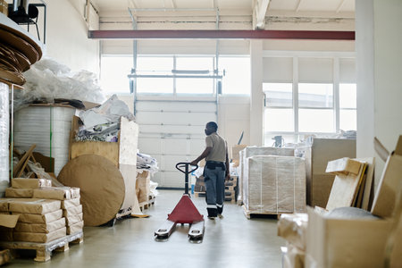 Wide shot of mature African American man working in print shop warehouse using pallet jackの写真素材