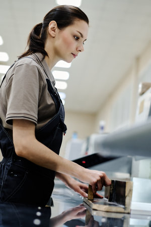 Vertical medium portrait of modern young female print shop worker preparing pile of paper for cuttingの写真素材