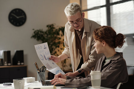 Young Caucasian woman and man discussing marketing issues while looking at printed graphs and charts