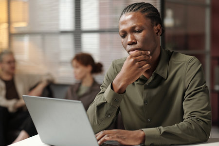 Pensive young African American manager looking at laptop screen, medium portrait