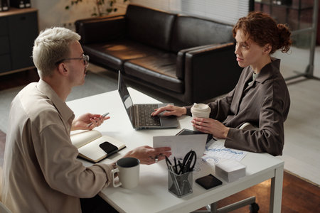 High angle of young gen Z male and female coworkers sitting at office desk in front of each other, discussing survey resultsの写真素材