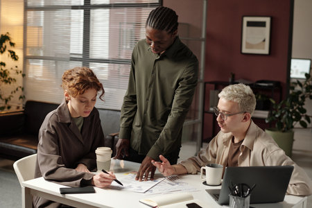 Group of three ambitious young coworkers discussing ideas while working on new project in modern...