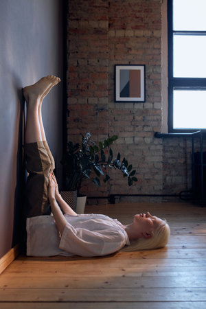 Vertical side view shot of young woman with albinism wearing casual outfit lying on floor with eyes...