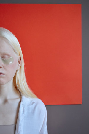 Vertical studio portrait of modern Caucasian woman with collagen patches under eyes standing against red and gray backgroundの写真素材