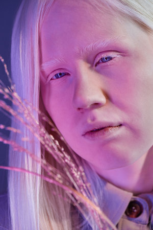 Vertical close-up shot of modern young Caucasian woman with albinism holding gilded plant standing...