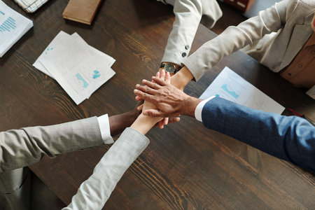 Diverse group of young adult and middle aged men and women stacking hands in teamwork gesture on...