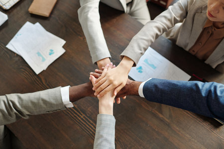 Diverse group of young adult and middle aged men and women stacking hands in teamwork gesture on...