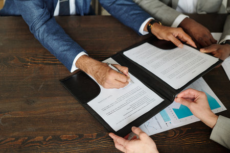 Caucasian middle aged man signing contract while Black middle aged man and Caucasian middle aged...