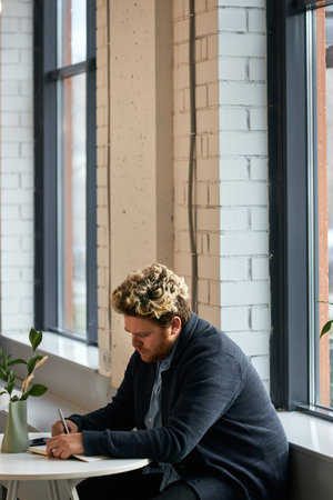 Vertical shot of handsome young Caucasian man spending lunch break in modern cafe waiting for order...