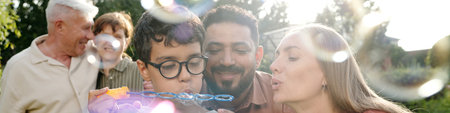 Multiethnic family of young parents, sons and senior couple blowing soap bubbles together outdoors,...