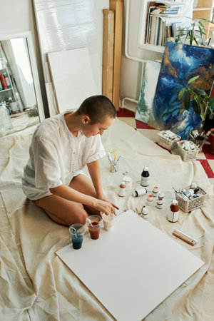 Vertical high angle shot of young Caucasian woman wearing white shirt sitting on floor in studio...
