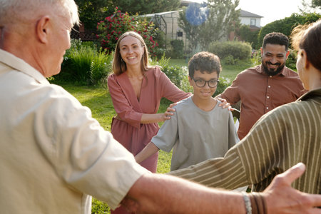 Multiethnic group including middle aged Caucasian man, young adult Caucasian woman, Middle Eastern man, teenage boy and middle aged woman standing outdoors holding hands in circleの写真素材