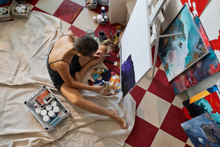 Horizontal from above view shot of professional artist sitting on floor in studio adding acrylic...