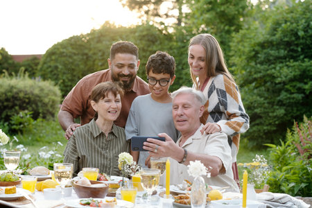 Multiethnic family group including senior Caucasian man, middle aged Caucasian woman, young adult Caucasian woman, young adult Middle Eastern man, preteen boy gathering outdoors taking selfieの写真素材