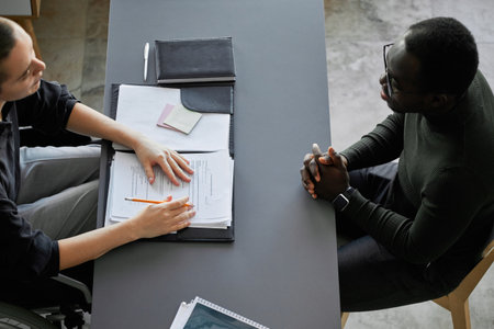 From above shot of young female HR specialist with disability sitting on wheelchair interviewing...