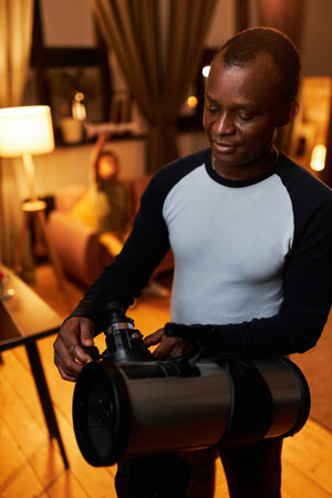 Vertical medium shot of African American man adjusting telescope settings to watch planets and stars with his sonの写真素材
