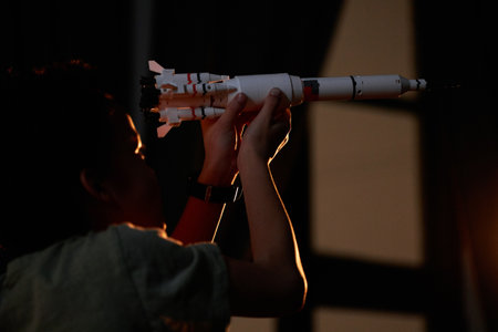 Medium close-up shot of joyful African American boy having fun playing with toy space rocket at nightの写真素材