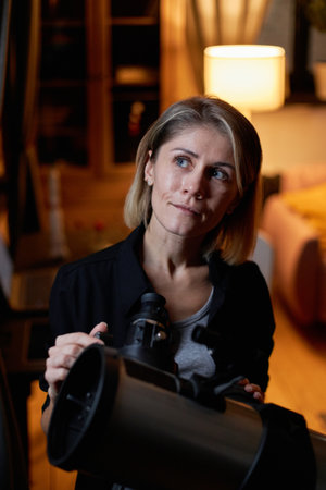 Vertical high angle of modern mature Caucasian woman learning astronomy standing in front of window looking at night skyの写真素材
