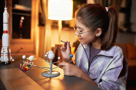 Portrait of happy Caucasian girl enjoying painting solar system model with acrylic paints for astronomy class project in evening at homeの写真素材