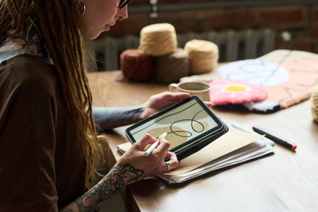 Young adult Caucasian woman with tattoos designing carpet pattern on digital tablet in carpet...
